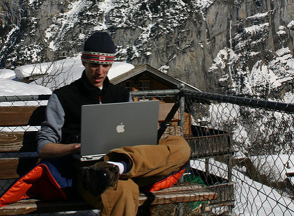 Young entrepreneur working on a laptop with snow-covered mountains in the background, representing modern startup life.