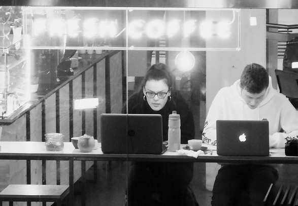 Two entrepreneurs working on laptops in a coffee shop, representing founders taking online startup courses and building businesses.